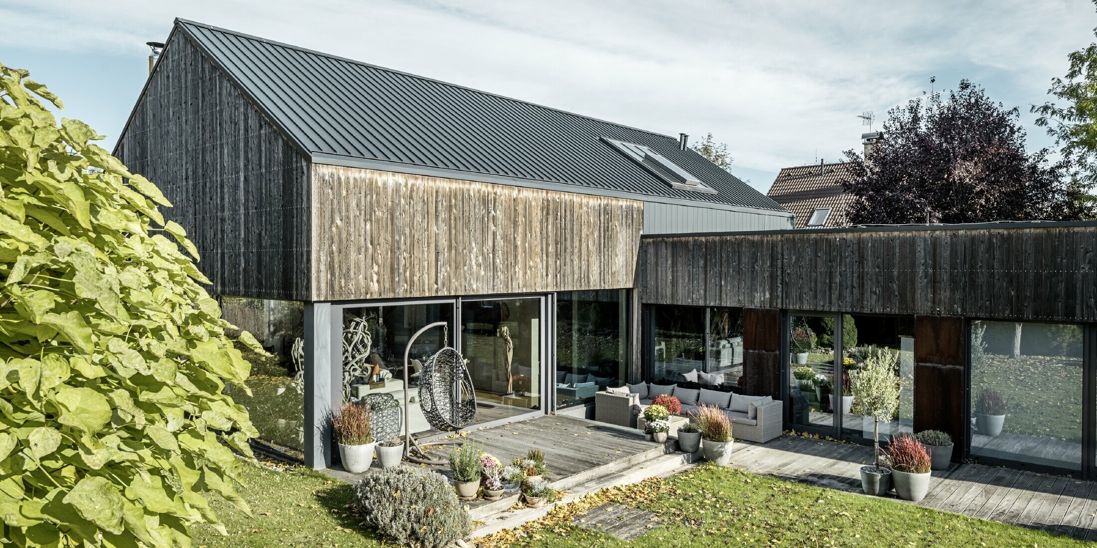 Casa unifamiliare con tetto a due falde, rivestito con aggraffatura doppia PREFALZ in antracite e facciata di legno invecchiata. Con una bella terrazza in legno e grandi finestre al piano terra.