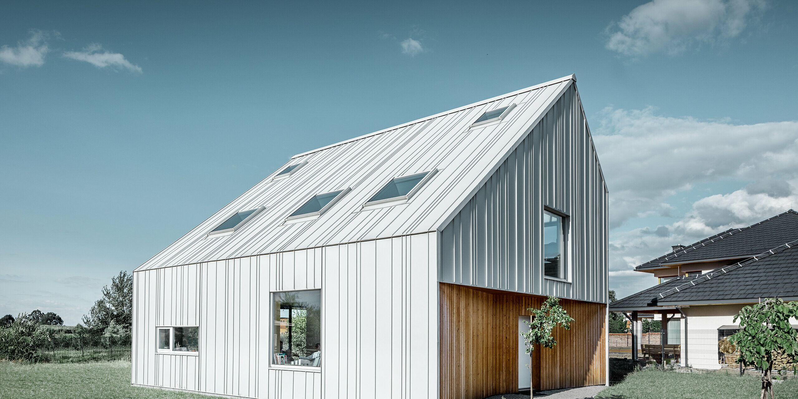 Casa unifamiliare dal taglio moderno con tetto a due falde, l’intero rivestimento esterno è realizzato con PREFALZ in bianco Prefa. Le diverse larghezze delle lastre si estendono dal tetto alla facciata. Sul tetto sono installati diversi lucernari.