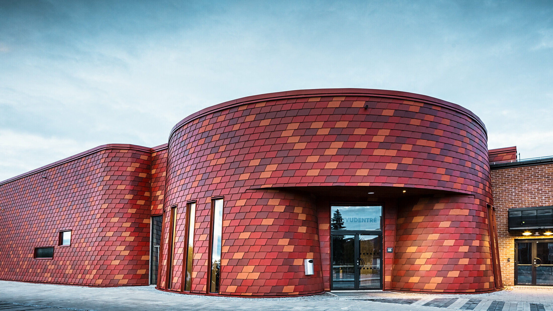 Große Eissporthalle mit abgerundeten Ecken. Die Fassade wurde mit Wandschindeln von PREFA in unterschiedlichen Rottönen verkleidet.