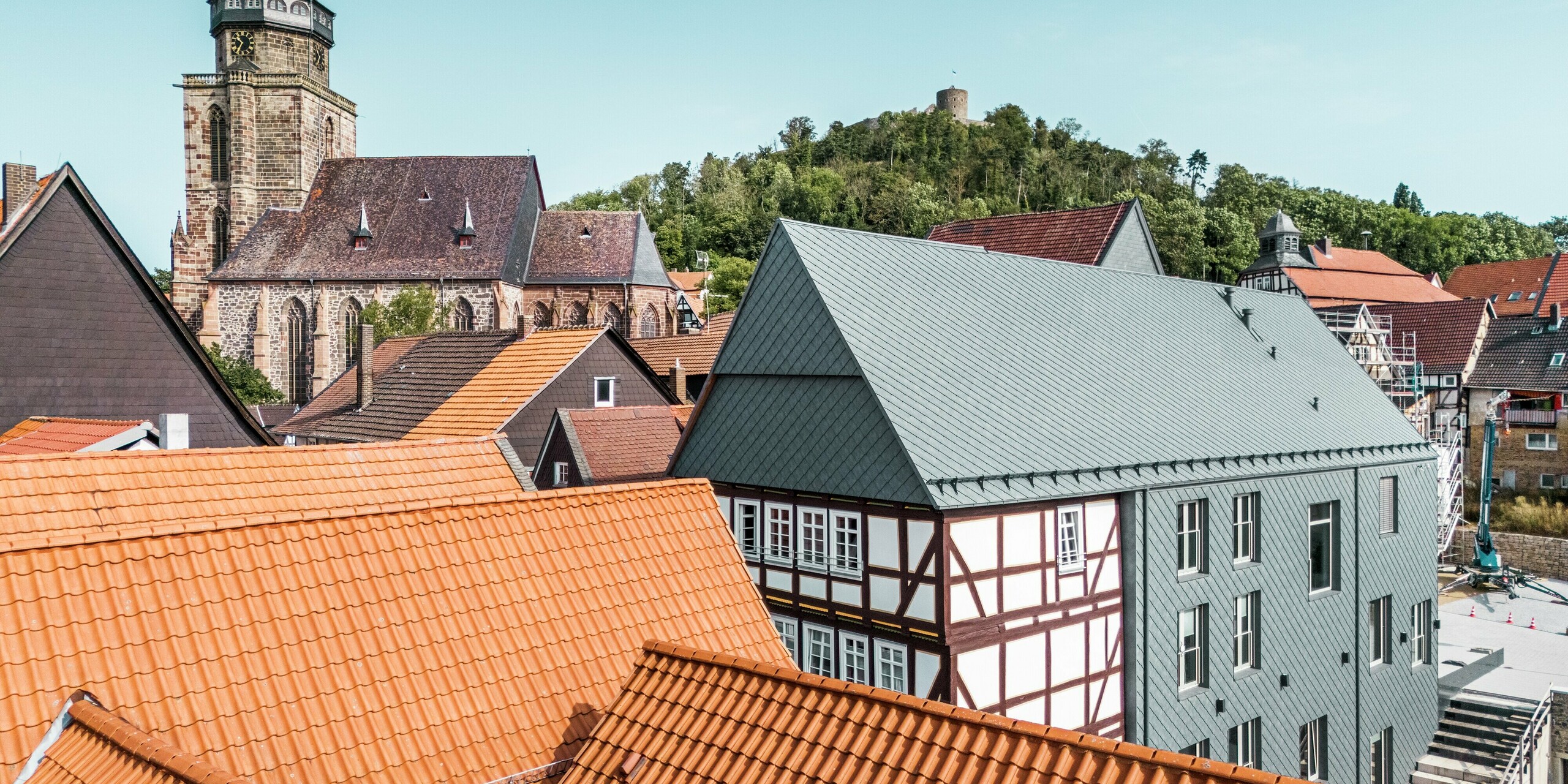 Drohnenaufnahme des sanierten Volkshauses in Homberg, Deutschland, mit moderner Aluminiumverkleidung. PREFA Dach- und Wandrauten 29 × 29 in P.10 Steingrau sorgen für zeitlose Eleganz, hohe Witterungsbeständigkeit und eine harmonische Symbiose mit der historischen Umgebung aus traditionellen Fassaden. 