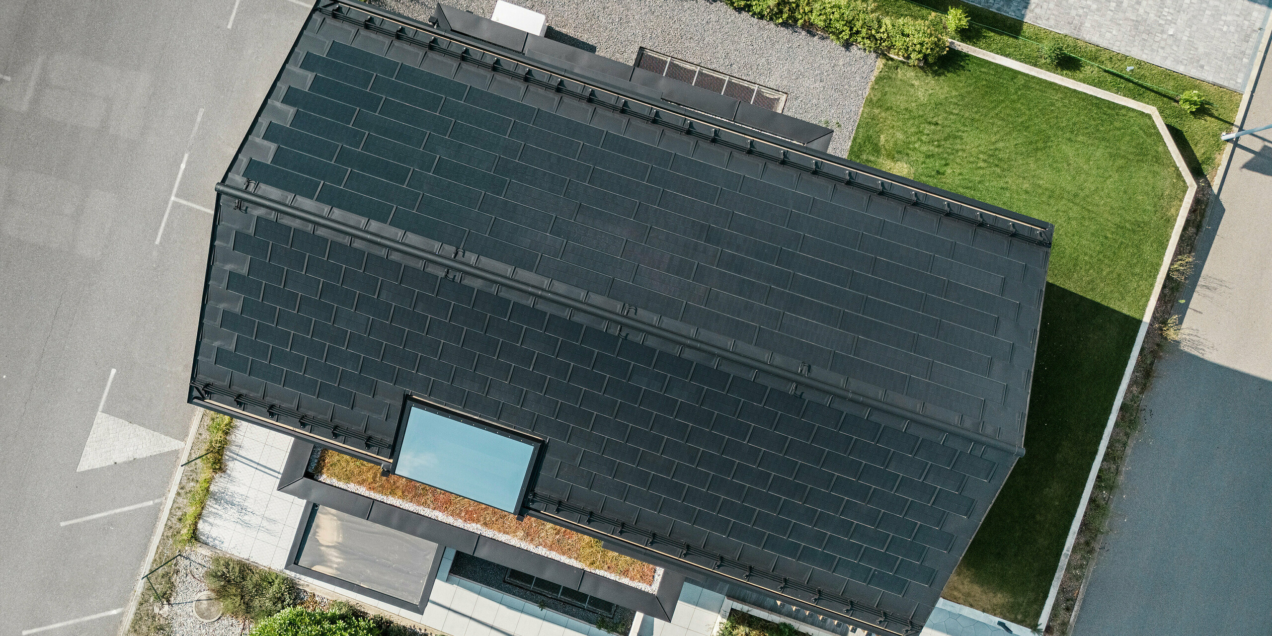 Vogelperspektive auf das Musterhaus Autark im Fertighauszentrum Blaue Lagune, Vösendorf (AT). Das Dach ist mit schwarzen PREFA Solardachplatten und Dachplatten R.16 in der hochwertigen Beschichtung P.10 eingedeckt. Das innovative Dachsystem mit integrierten Photovoltaikmodulen sorgt für eine beeindruckende Optik und nachhaltige Energiegewinnung aus Sonnenenergie.