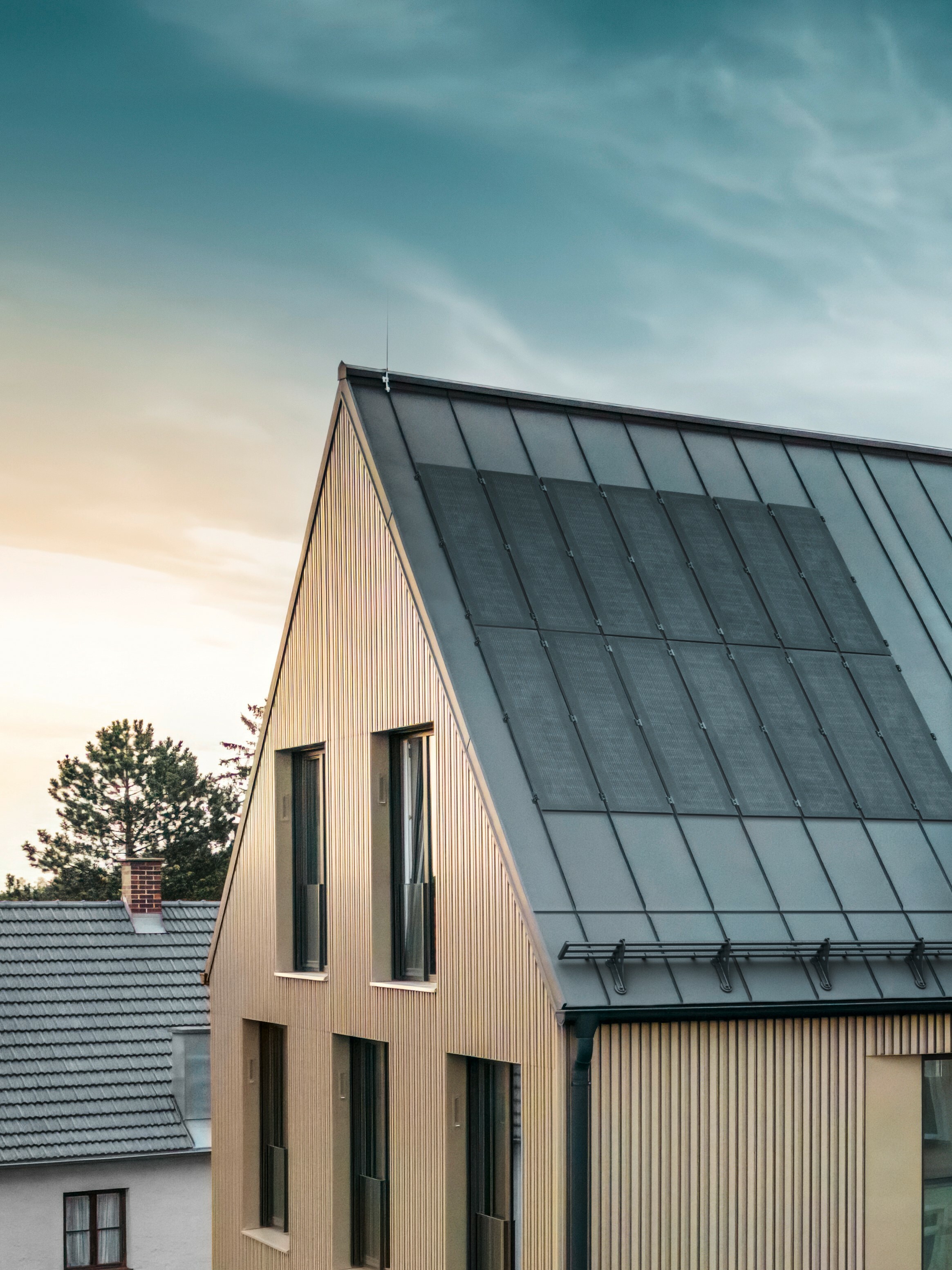 On y voit un bâtiment avec une façade PREFALZ bronze. Les modules solaires PREFALZ innovants, dotés de la toute dernière technologie de cellules TOPCon, installés sur le toit gris noir de PREFALZ, assurent une production d'énergie durable.