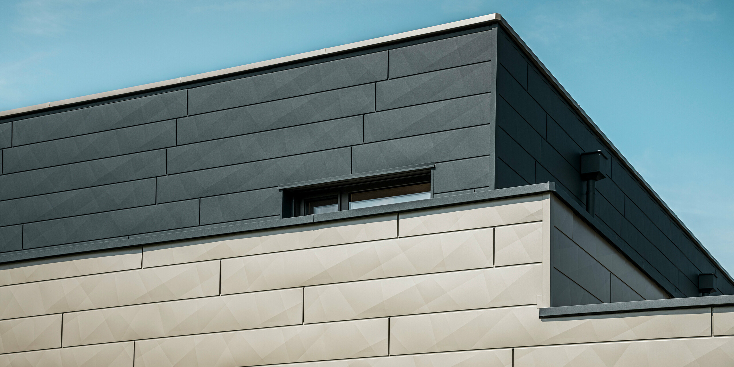 Gros plan de la façade en aluminium PREFA bicolore d'une maison unifamiliale moderne à Wippenham, en Autriche. La façade est conçue avec des panneaux de façade Siding.X en anthracite et bronze, qui créent une apparence élégante et dynamique. Le travail précis et le jeu des couleurs soulignent l'architecture contemporaine du bâtiment.