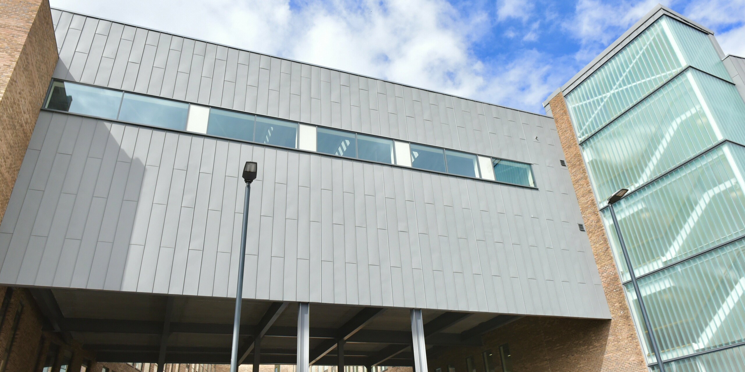 Bâtiment pont du North Regional College à Coleraine avec façade aluminium PREFALZ en gris quartz. La toiture innovante à joint debout confère à l'établissement d'enseignement légèreté et robustesse à la fois. La façade en aluminium et brique harmonise et confère au bâtiment une architecture intemporelle.