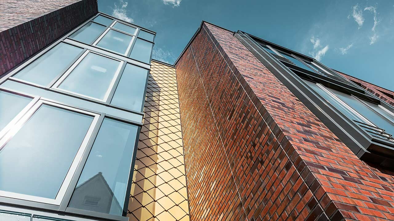 Facciata concava con scaglia a muro flessibile rivestito in alluminio in Mayagold, großzügige Glasflächen und einer Klinkerfassade an dem neuen Schuhhaus Schüttfort in Hamburg-Bergedorf