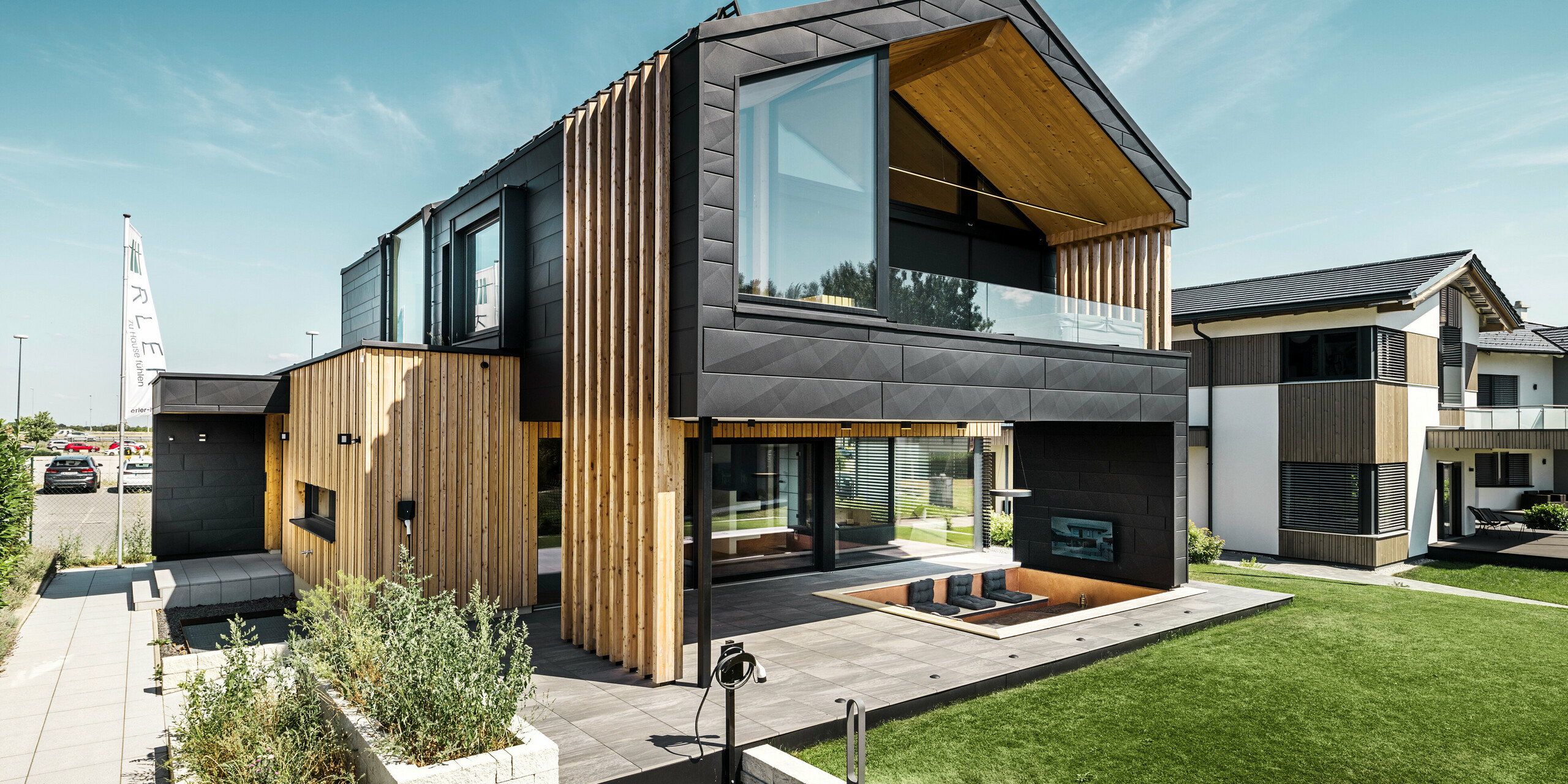 Le côté jardin de la maison témoin Autark du centre de maisons préfabriquées Blaue Lagune à Vösendorf (AT) présente une combinaison moderne de panneaux de façade PREFA Siding.X en P.10 noir et d'éléments en bois naturel. Le design combine de généreuses façades vitrées à l'étage supérieur et une terrasse couverte avec un coin salon intégré au rez-de-chaussée. Les deux étages s'intègrent harmonieusement l'un dans l'autre et créent une atmosphère de vie luxueuse.