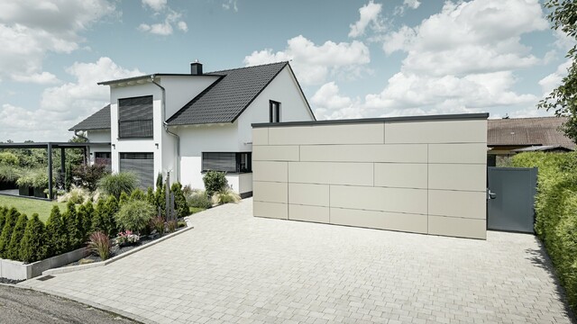 Die Garage des Einfamilienhauses ist an der Fassade komplett mit der Aluminium Verbundplatte in Bronze verkleidet. Auch das Garagentor ist mit den Fugen nicht erkennbar. Davor ist eine großzügige Einfahrt. 