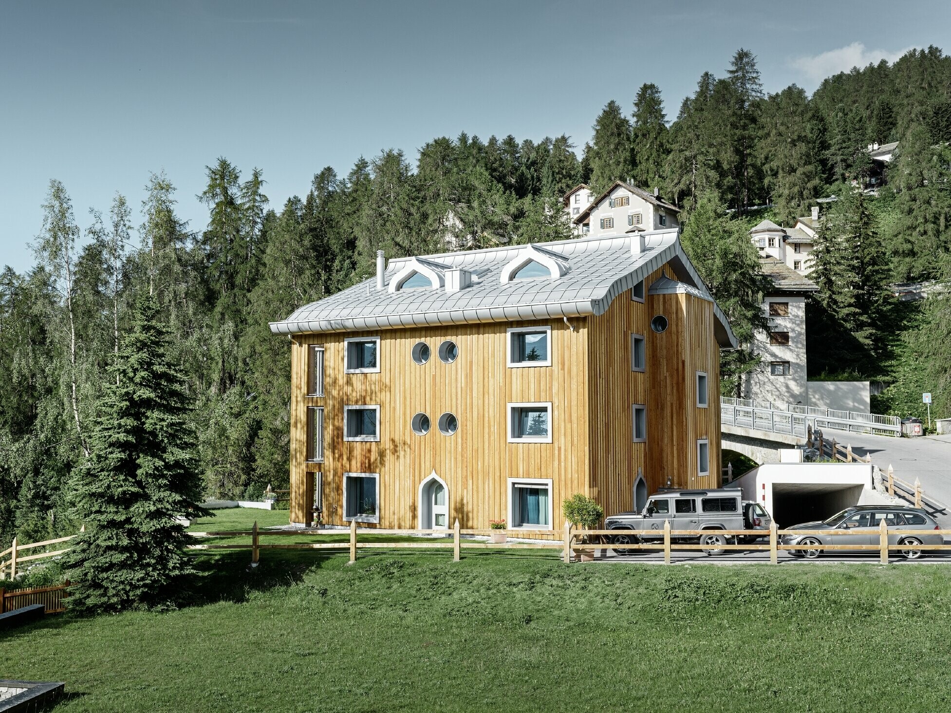 Wohnhausanlage in St. Moritz mit Holzfassade und Aluminiumdach mit geschwungener Traufe in silbermetallic