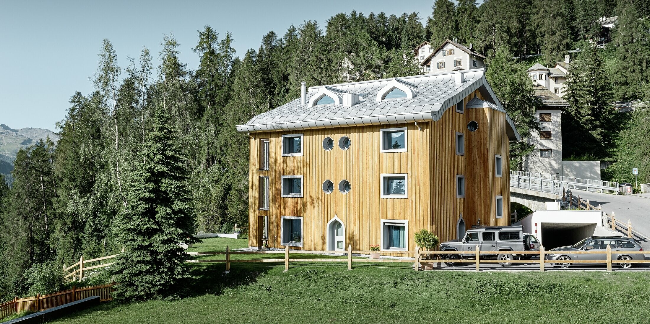 Wohnhausanlage in St. Moritz mit Holzfassade und Aluminiumdach mit geschwungener Traufe in silbermetallic