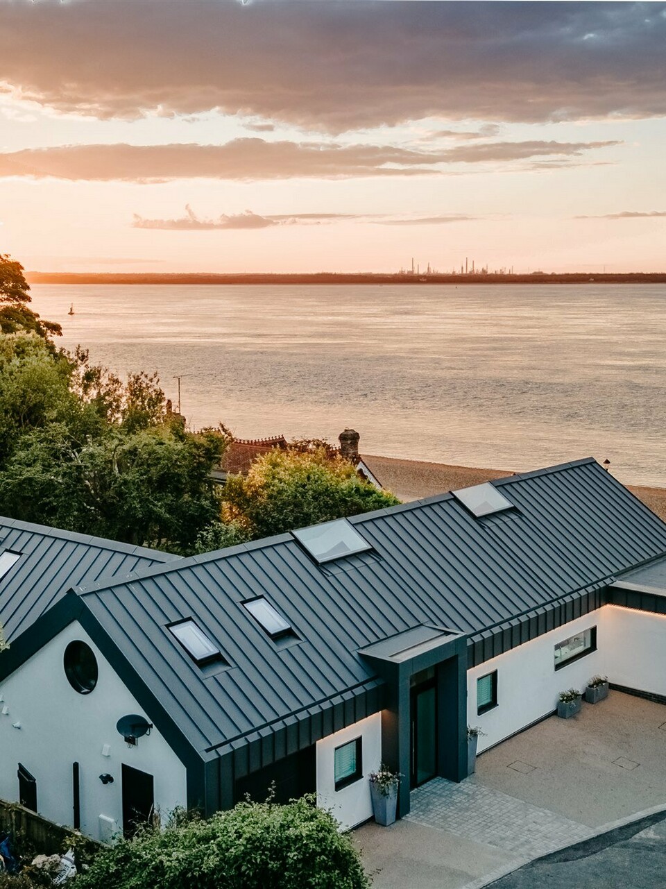 Ein luxuriöser Bungalow auf Isle of Wight, in der Nähe von Bournemouth, wurde mit PREFALZ in der Farbe P.10 Dunkelgrau eingedeckt und fügt sich harmonisch in natürliche Umgebung ein. Das moderne Gebäude mit der eleganten Aluminiumhülle, die mit einer weißen Putzfassade kombiniert wurde, vermittelt ein klares und unaufgeregtes Design. Das architektonische Highlight an der Südküste Englands liegt direkt am Meer. Im Hintergrund wird eine malerische Kulisse in der Golden Hour, der Stunde des Sonnenuntergangs, präsentiert.