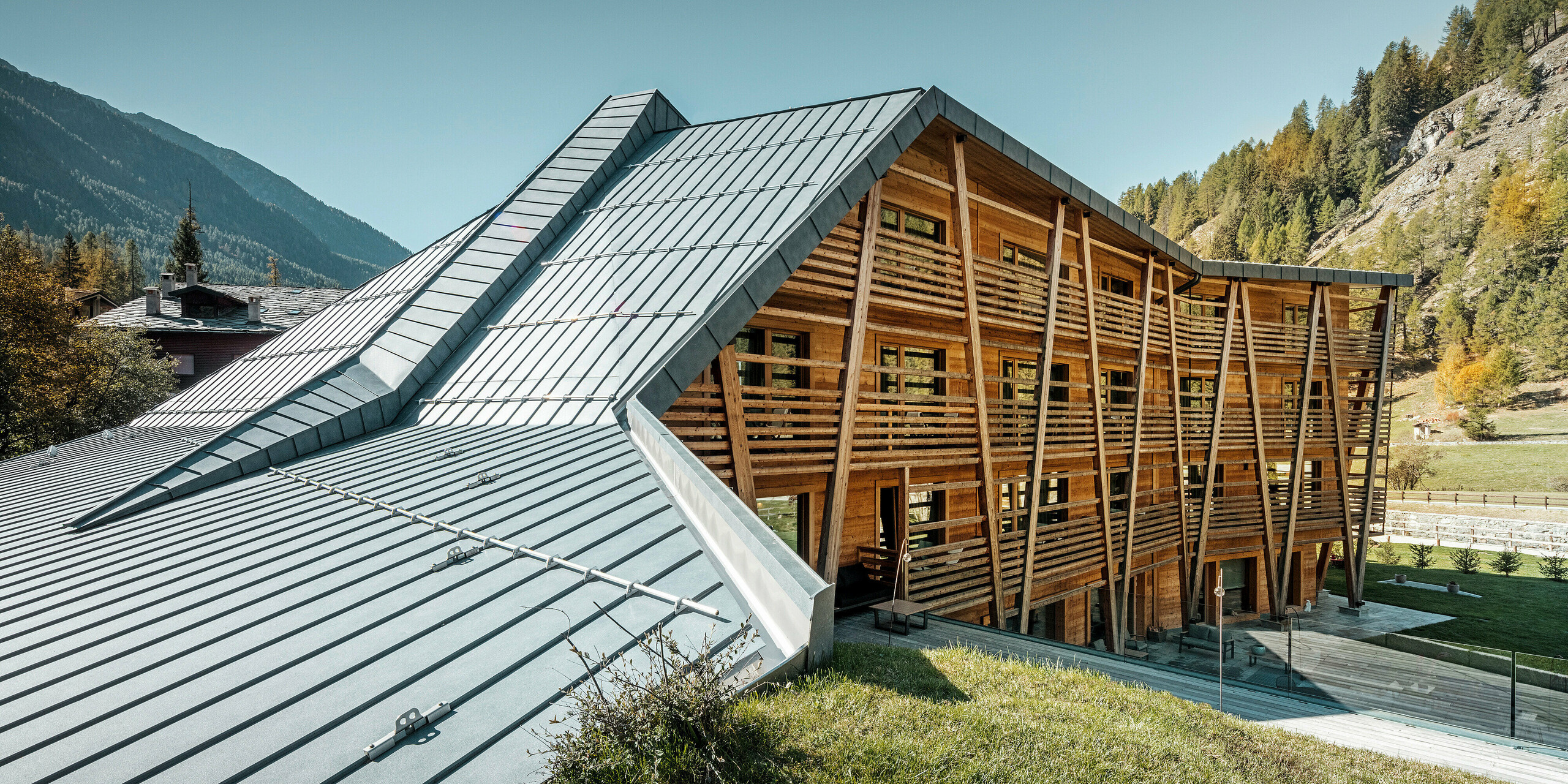 Das Hotel 'Au Charmant Petit Lac' in Champoluc zeigt eine einzigartige architektonische Harmonie, bei der das PREFALZ Dachsystem in P.10 Steingrau gekonnt mit der holzverkleideten Struktur des Gebäudes verschmilzt. Die dynamische Dachgestaltung mit ihren klaren Linien und Falzen fügt sich nahtlos in die umliegende Alpenlandschaft ein und bietet einen modernen Kontrast zur traditionellen Holzbauweise. Diese Kombination aus modernen und natürlichen Materialien spiegelt das Engagement des Hotels für umweltbewusstes Design und Nachhaltigkeit wider.