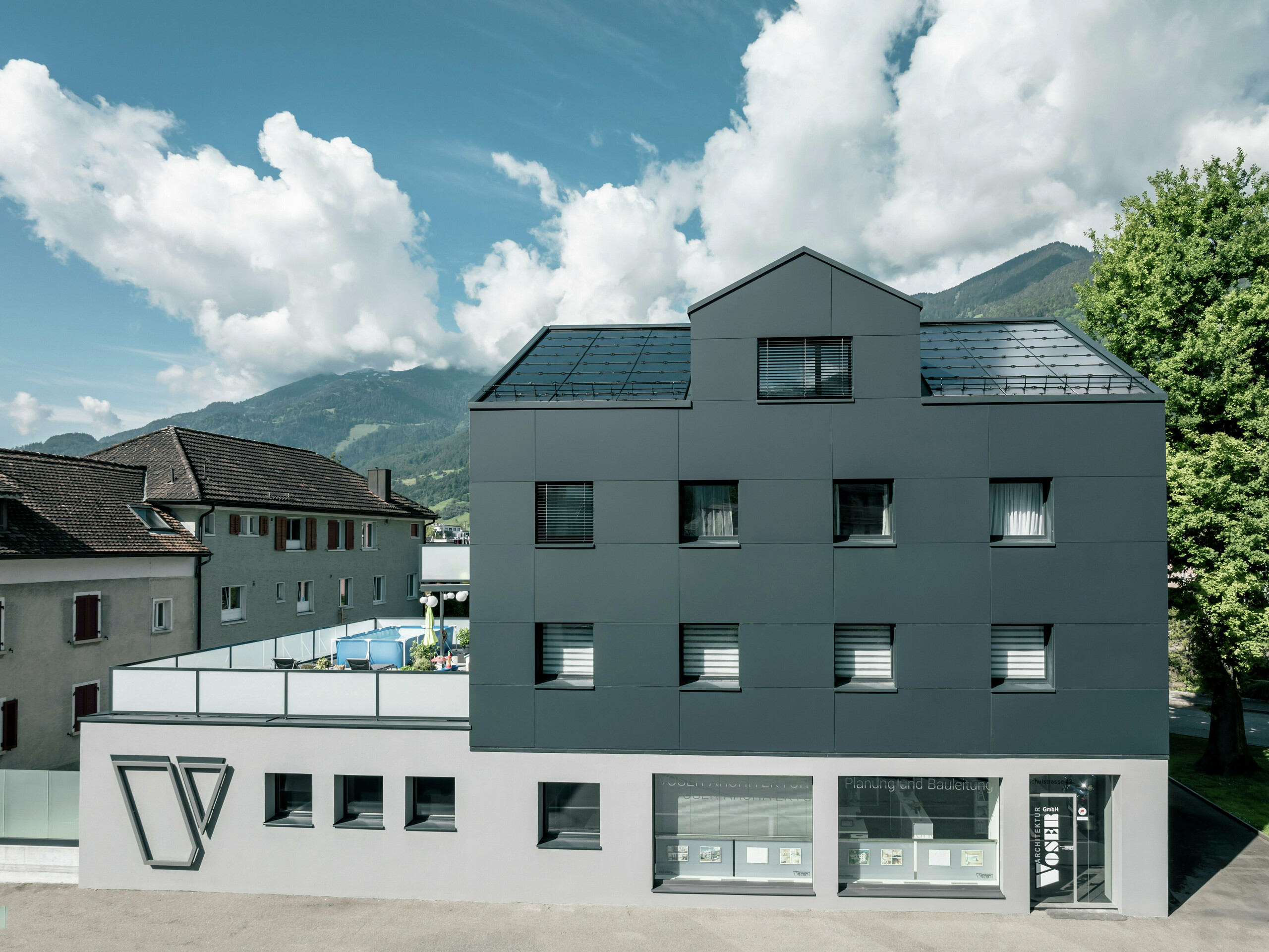 Frontalansicht eines sanierten Geschäftsgebäudes nach der Fassadensanierung mit PREFABOND Aluminium-Verbundplatten in Anthrazit. Die klare und hochwertige Fassade verleiht dem Gebäude eine elegante und zeitgemäße Optik. Im Erdgeschoss befinden sich große Fensterflächen, die das Architekturbüro Voser repräsentieren.