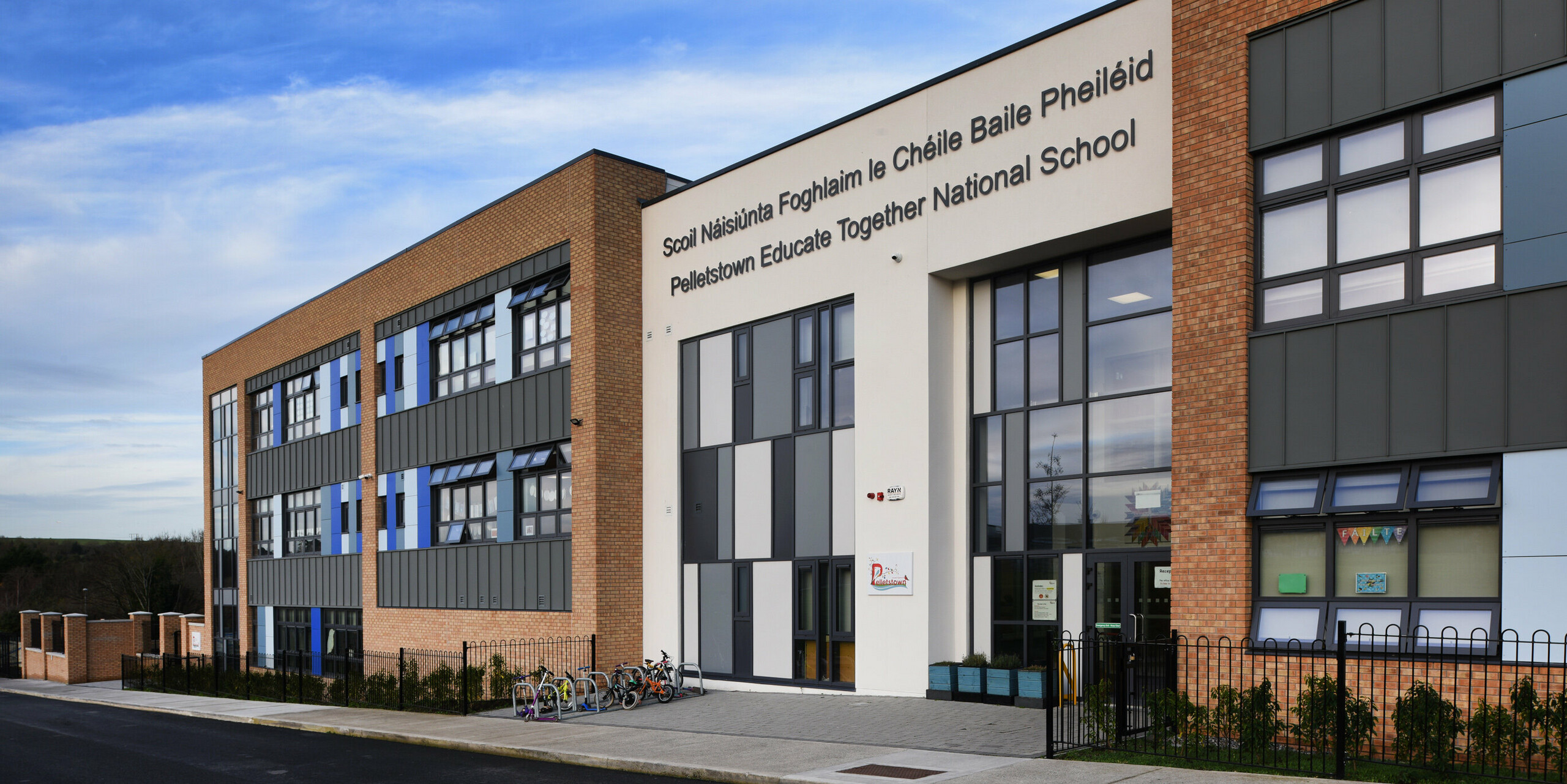 Vue détaillée de l'entrée principale de Pelletstown Educate Together National School à Dublin. La façade en aluminium en PREFALZ P.10 gris souris en combinaison avec du crépi et des briques crée une apparence unique et offre à l'école une enveloppe de bâtiment durable et esthétique.