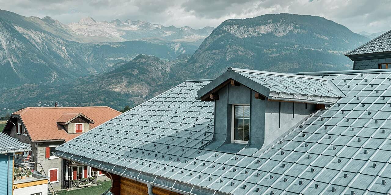 Toit à deux pans avec lucarne ; le choix s’est porté sur la toiture en tôle de PREFA et la tuile couleur gris pierre. La lucarne est habillée d’une couverture à joint debout de PREFA couleur gris pierre.