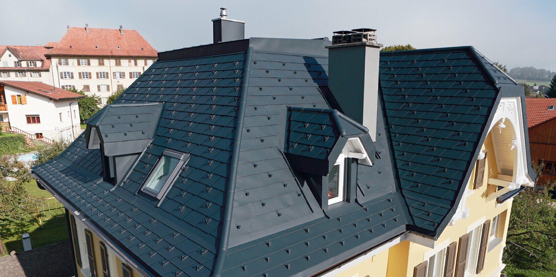 Villa in der Schweiz, das Dach hat viele Kehlen und kleine Gauben, das Dach ist mit einer Alu Schindel von PREFA eingedeckt in P.10 Anthrazit