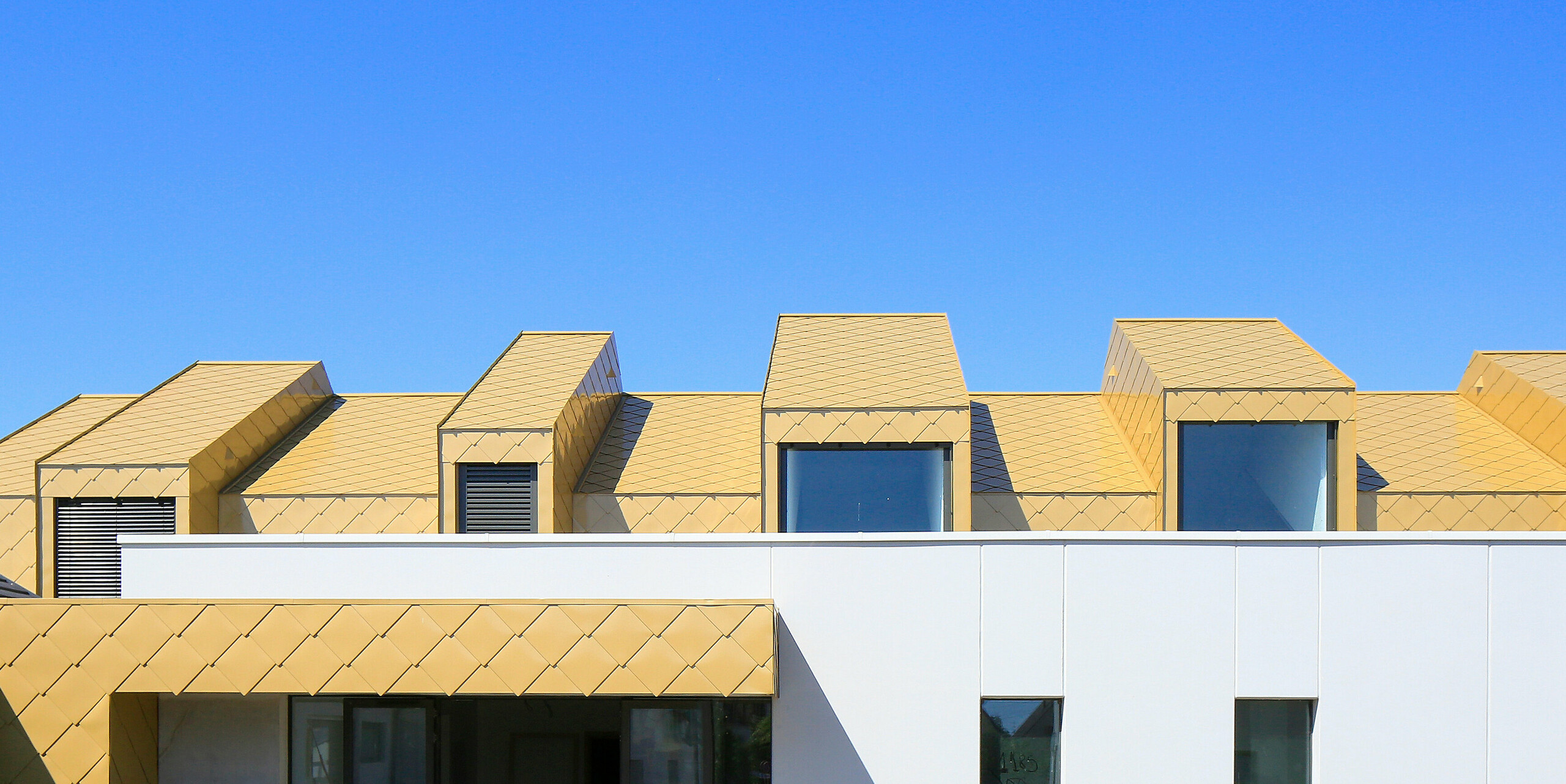 Le toit et la façade du dernier étage du Centre Communautaire et Culturel de Fessenheim, en France, ont été recouverts de losanges de toiture et de façade PREFA 44 × 44 en Sparkling Gold.