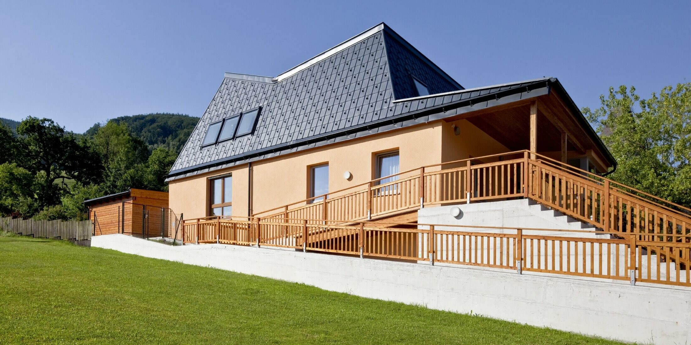 Kindergarten mit oranger Putzfassaade und verwinkeltem Dach, gedeckt mit der PREFA Dachplatte in P.10 Anthrazit;