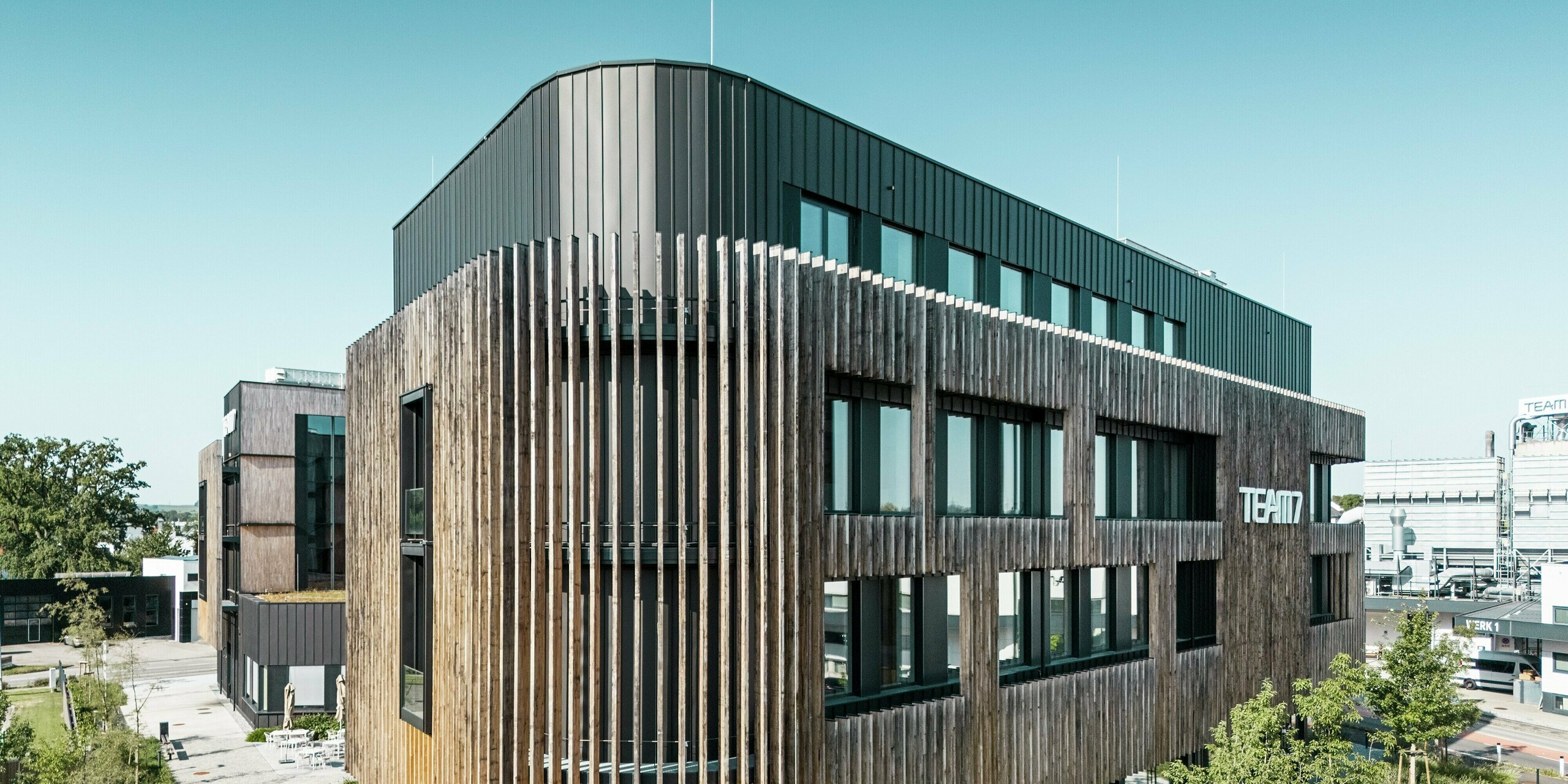 Le Team 7 World à Ried im Innkreis (Haute-Autriche) combine une façade PREFALZ noir-brun avec des éléments verticaux en bois, de grandes fenêtres et de généreux espaces verts. La combinaison d'un revêtement en aluminium durable et de bois naturel crée une combinaison harmonieuse de durabilité, de design moderne et de fonctionnalité. Une symbiose parfaite entre architecture, nature et construction innovante.