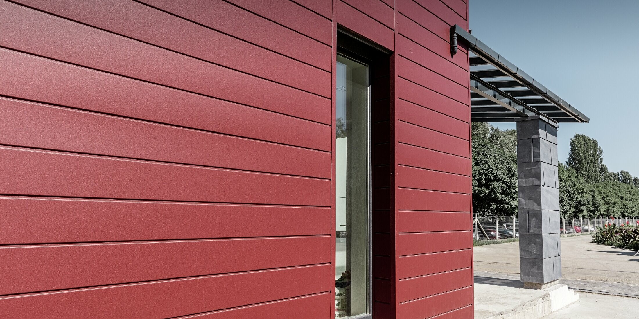 Modernes Bürogebäude mit einer geteilten Fassade in rot, steingrau und weiß mit Aluminiumprodukten Sidings, Fassadenpaneel FX.12 und Aluminium Verbundplatte von PREFA