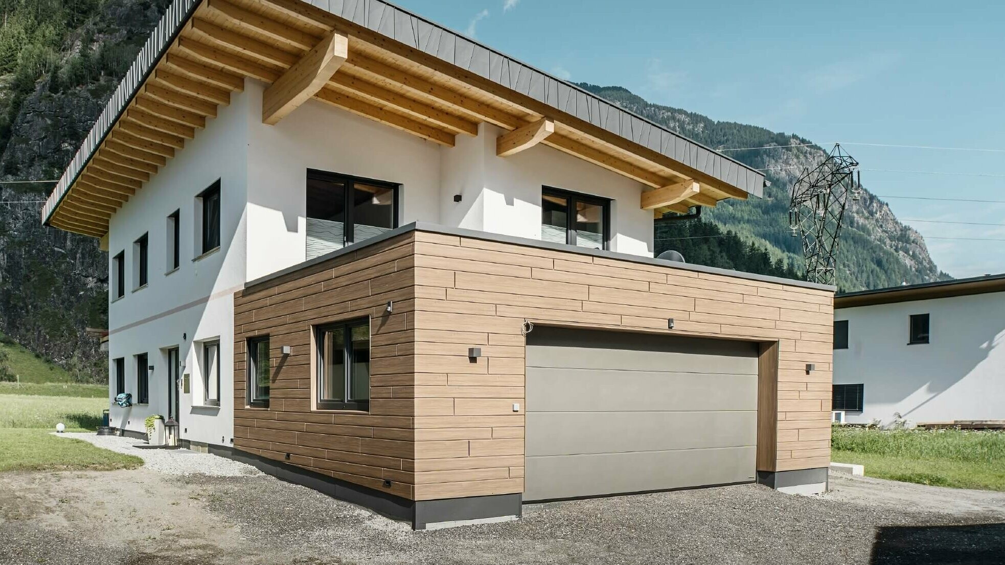 Garage eines Wohnhauses mit PREFA Sidings in Holzoptik im Farbton "Walnuss Braun". Im Hintergrund sind Berge zu sehen. 