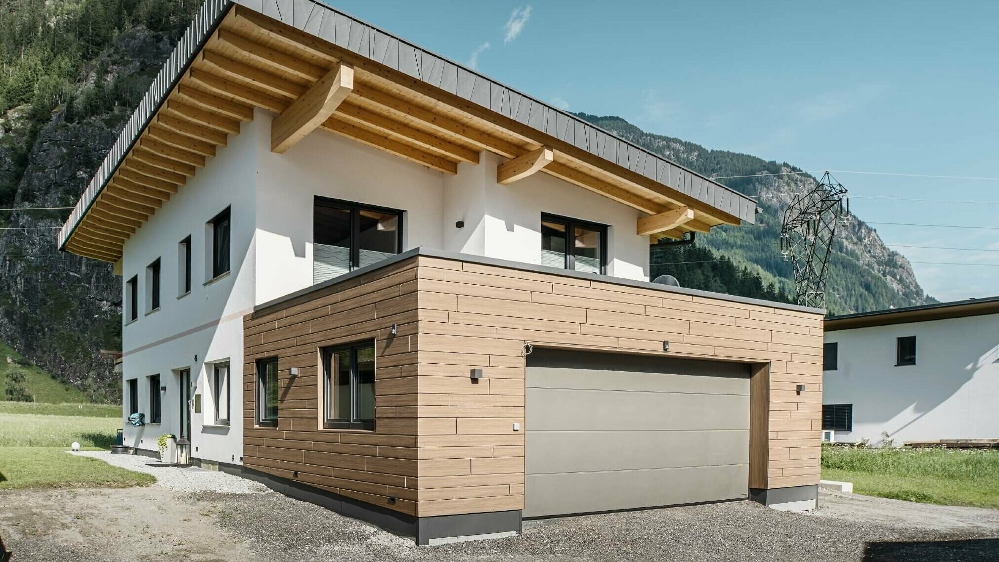 Garage di una palazzina con doghe PREFA effetto legno di colore "noce scuro". Sullo sfondo si vedono le montagne. 