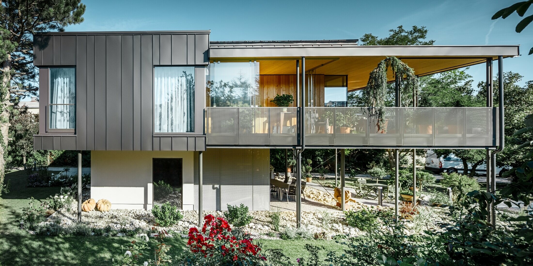 modernes Einfamilienhaus, ähnlich einem Baumhaus umgeben von einem großen Garten mit vielen Bäumen mit einer dezenten Winkelstehfalzfassade in schwarzgrau von PREFA