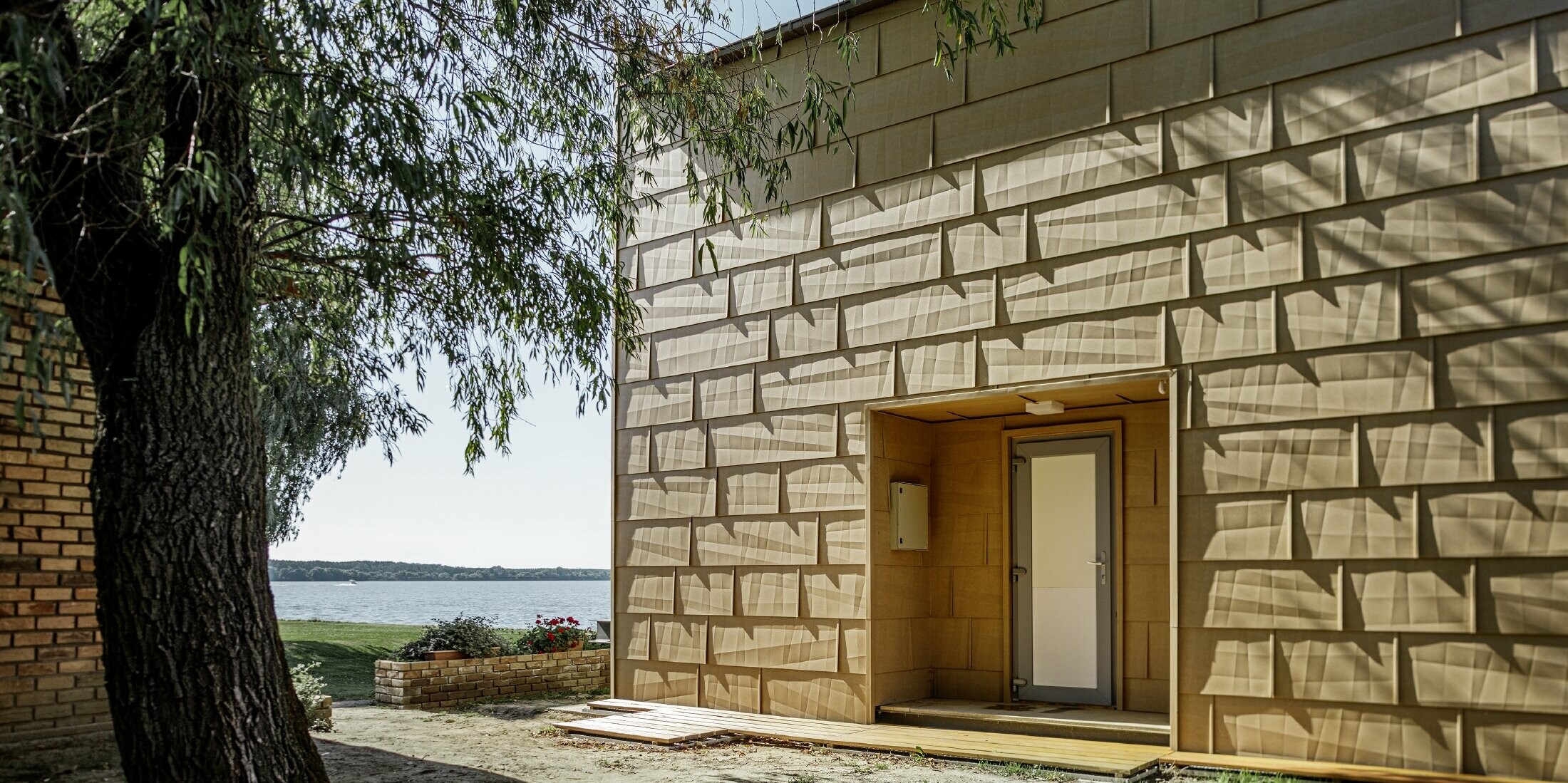 modernes Wochenendhaus mit Flachdach und großen Fensterflächen am See mit einer gekanteten Aluminiumfassade in sandbraun