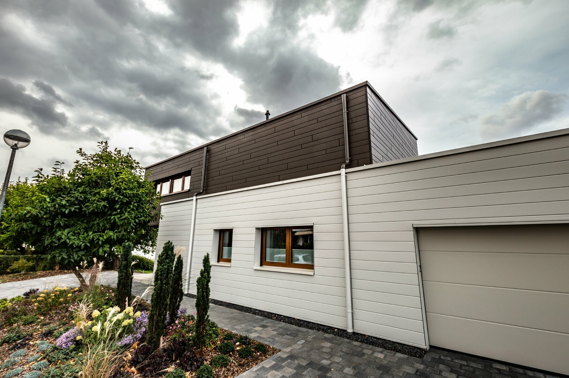 Rivestimento della facciata di un garage con doghe PREFA orizzontali di colore bianco, con grondaia con sbocco.