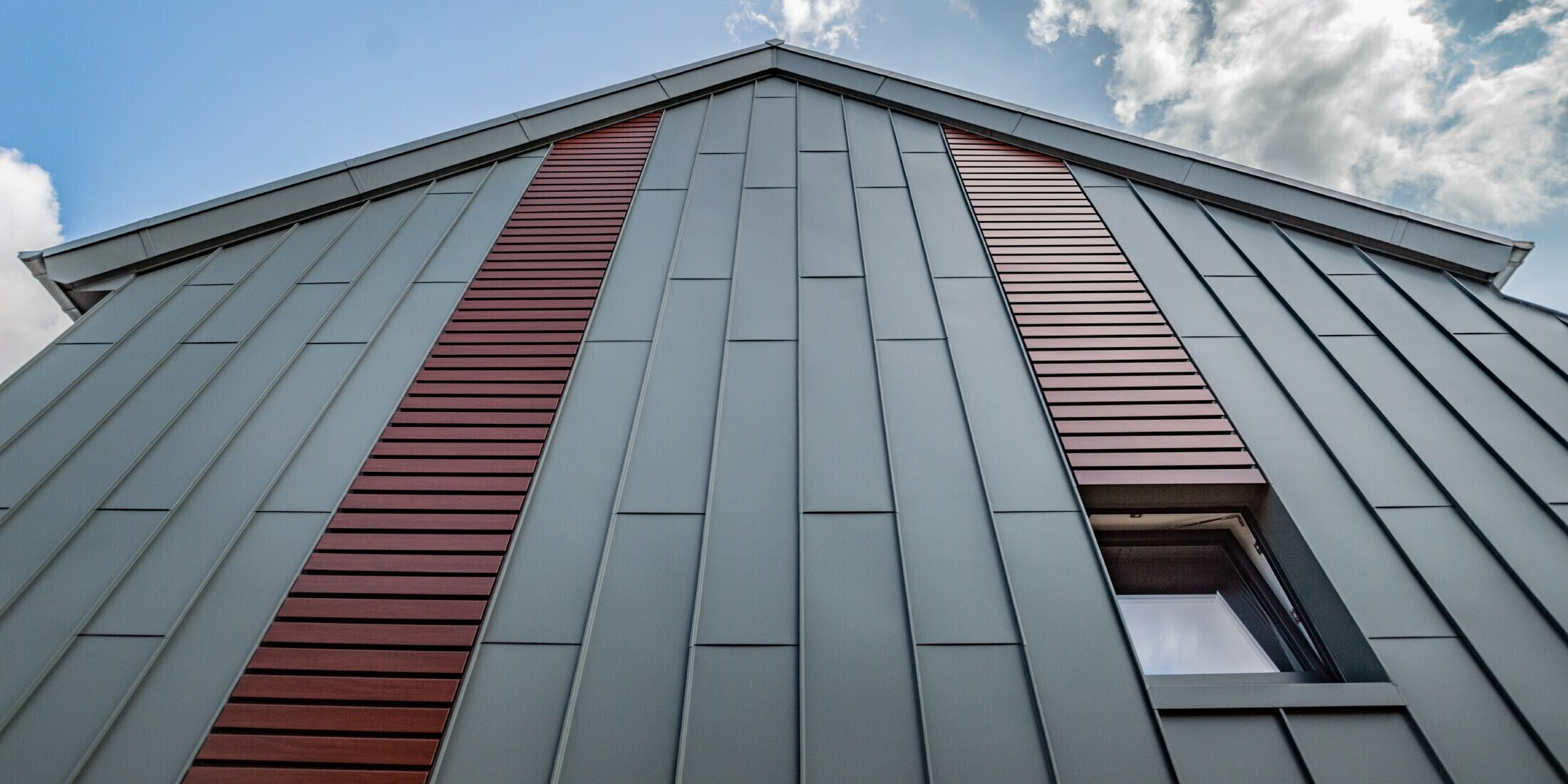 Vertikale Winkelstehfalzfassade mit Tafeldeckung in Hellgrau, sowie Siding horizontal in Holz dunkel von PREFA.