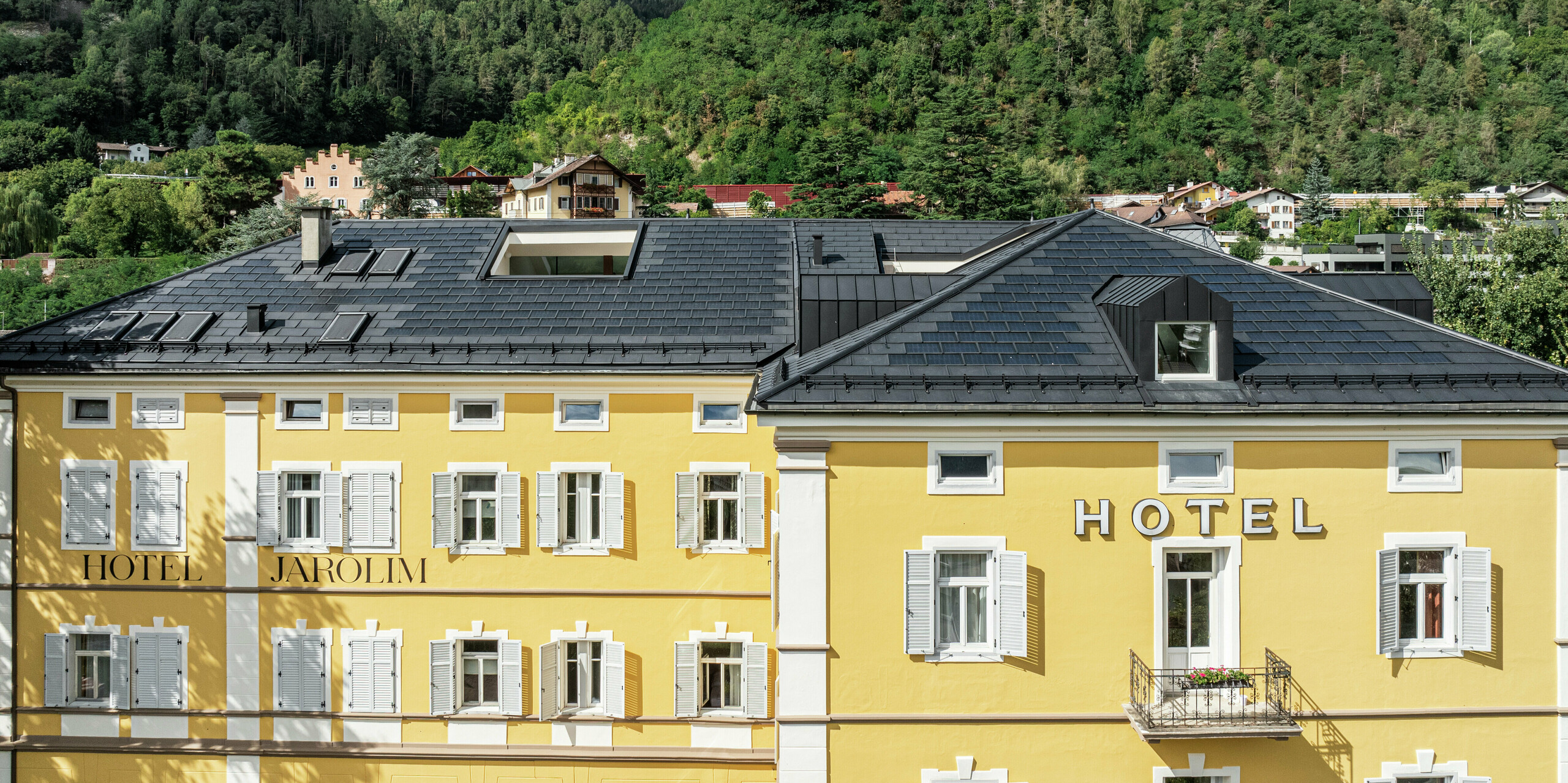 Das Hotel Jarolim in Brixen präsentiert sein neues Dach aus PREFA Solardachplatten und Dachplatten R.16 in zeitlosem P.10 Schwarz. Die Dachlösung vereint Robustheit, Witterungsbeständigkeit und Leichtigkeit, ideal für denkmalgeschützte Gebäude. Integrierte Photovoltaikmodule erzeugen umweltfreundlichen Strom, ohne die historische Optik zu beeinträchtigen. Passgenaue Gauben und Dachdetails unterstreichen die hohe Verarbeitungsqualität und ästhetische Vielseitigkeit der PREFA Aluminiumprodukte.