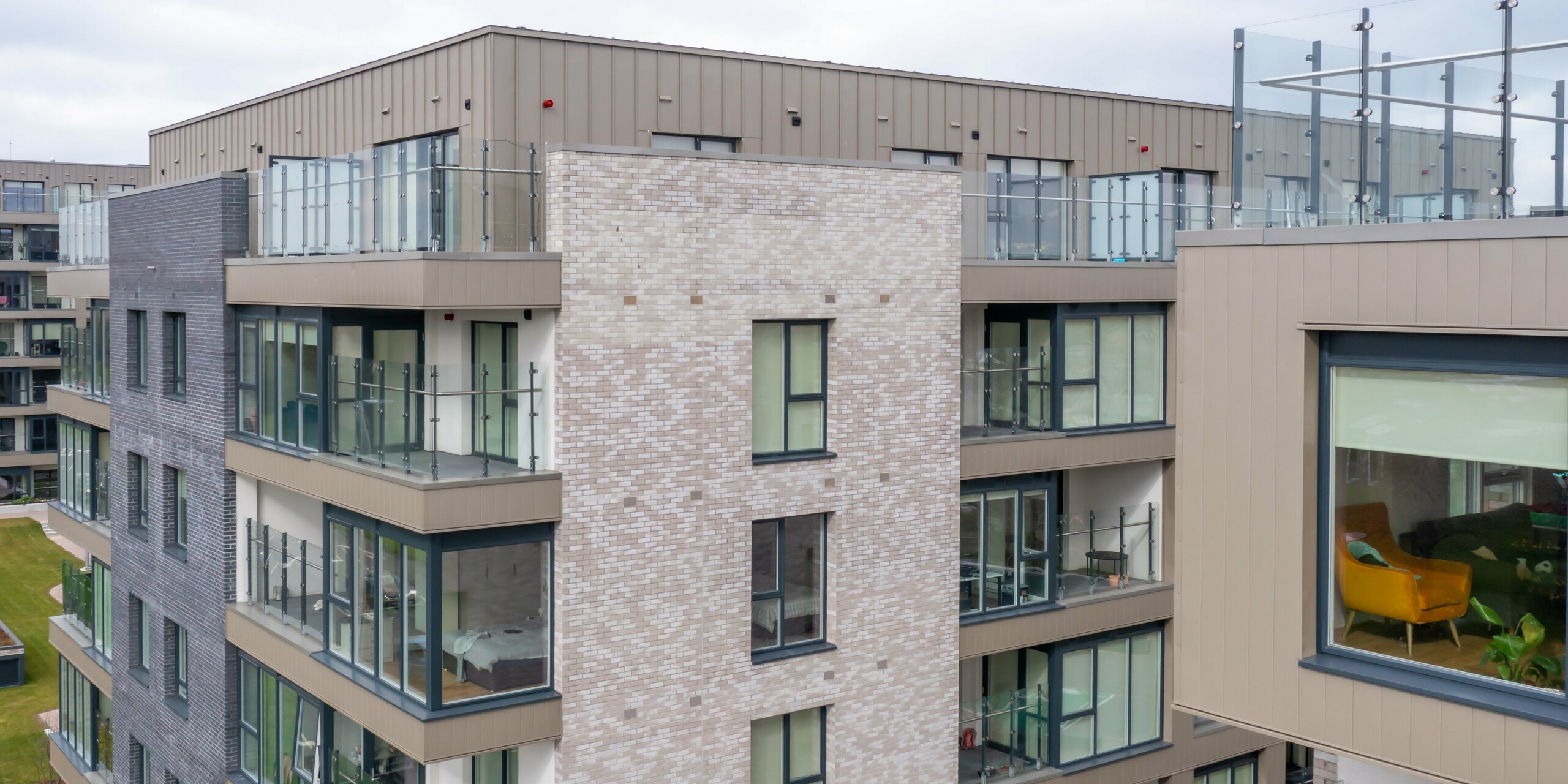 Prise de vue par drone du complexe résidentiel Palmers Gate à Palmerstown, Dublin, Irlande - Vue détaillée d'un immeuble résidentiel avec parements PREFA de couleur bronze et système de façade PREFALZ. La façade combine un bardage en aluminium avec des éléments en brique et de grandes baies vitrées. Les balcons sont équipés de balustrades en verre et offrent une qualité de vie moderne. Le complexe immobilier comprend plusieurs blocs résidentiels avec environ 1 700 m² de revêtements PREFA et environ 1 200 m² de systèmes de façade PREFALZ, connus pour leur longévité et leur design esthétique.