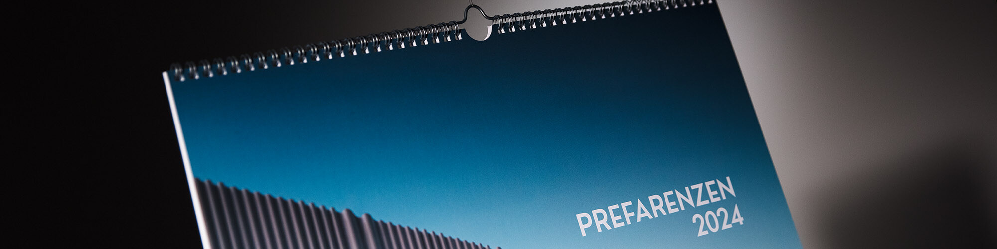 Une partie de la couverture du calendrier vue de près ; on peut voir une partie d'une façade ondulée en aluminium ainsi que l'inscription PREFARENZEN 2024.