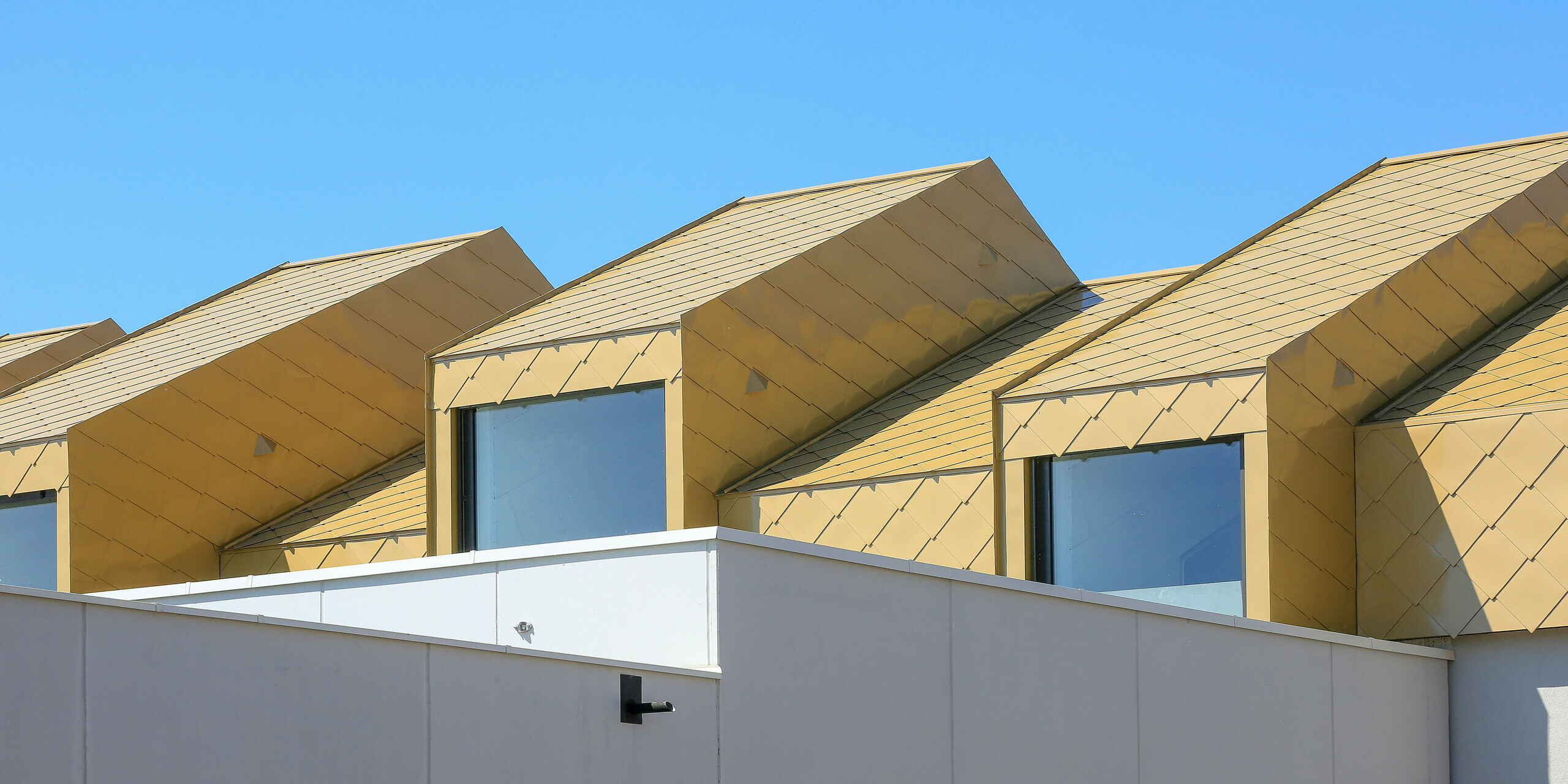 Vue depuis la rue du Centre Communautaire et Culturel de Fessenheim (France). Le dernier étage et le toit du bâtiment ont été revêtus de losanges de toiture et de façade PREFA 44 × 44 en Sparkling Gold.