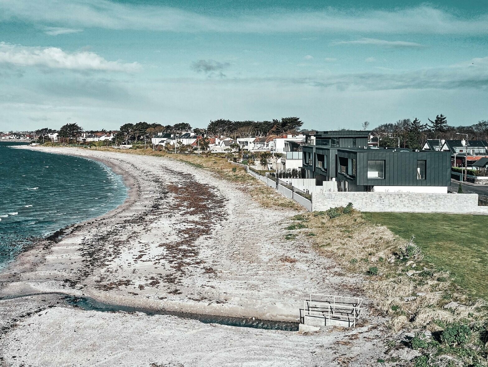 Bild der Wohnhäuser am Strand. Auf der linken Seite sieht man das Meer, auf der rechten Seite sind die Reihenhäuser zu sehen.