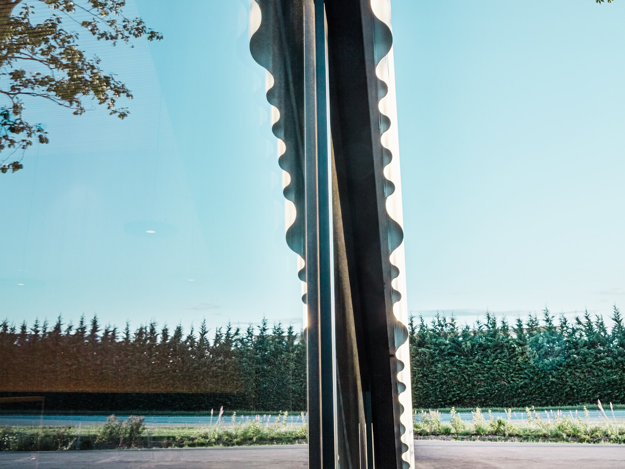 Un détail du restaurant Walters, sur lequel on peut voir une partie d'une fenêtre en arc de cercle et la finition de la façade ondulée. Les arbres des environs se reflètent dans le vitrage.