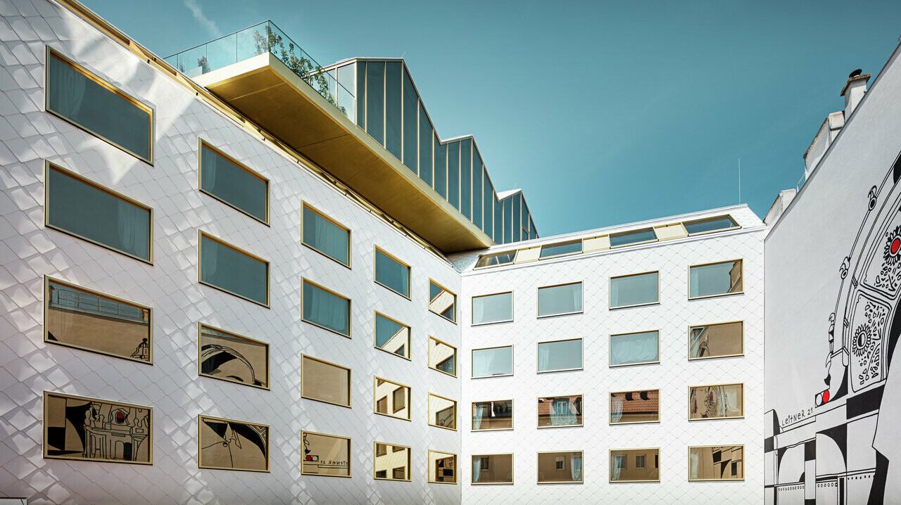 Perspektivische Ansicht des "THE ROCK Radisson RED Vienna" Hotels in Wien, gekennzeichnet durch seine innovative PREFA Aluminiumfassade mit Dach- und Wandrauten 44 × 44 in P.10 Reinweiß. Die unregelmäßig angeordneten Fenster mit Spiegelverglasung reflektieren dynamisch die Umgebung.