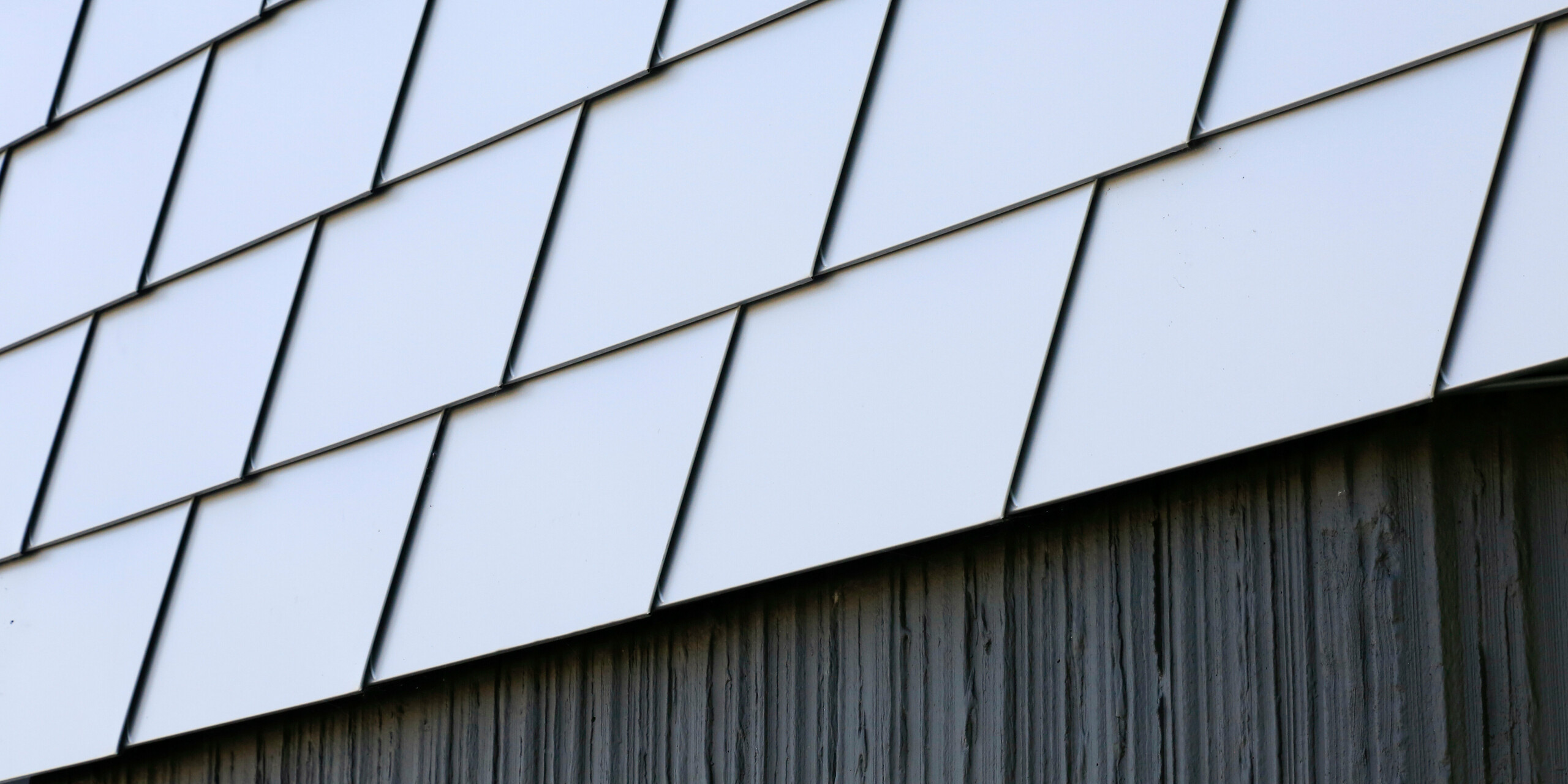Vue détaillée de la base du bâtiment en béton et de la façade en bardeaux PREFA couleur argent métallisé au centre de santé du Landreau