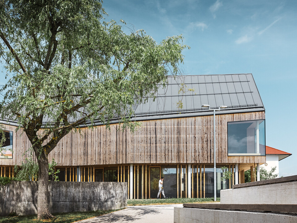 Das neue Pfahlbautenmuseum mit seiner Holzlamellenfassade und dem komplexen, dunkelgrauen PREFA Dach von der Seite; ein Baum rahmt den Bau links oben ein.