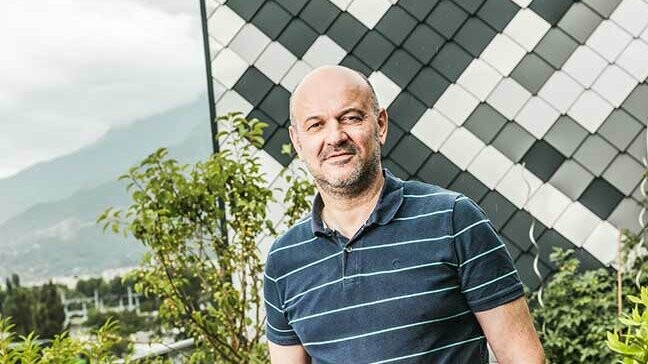 Portrait de l'artisant Patrick Gaide devant son bâtiment prestigieux en losange de  façade en aluminium PREFA vêtu d'un polo foncé