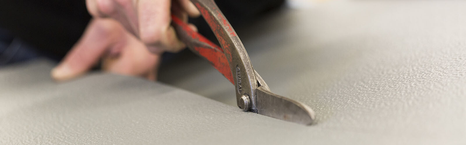 Ein Teilnehmer der PREFA Academy schneidet mit einer Blechschere präzise eine Aluminiumplatte. 