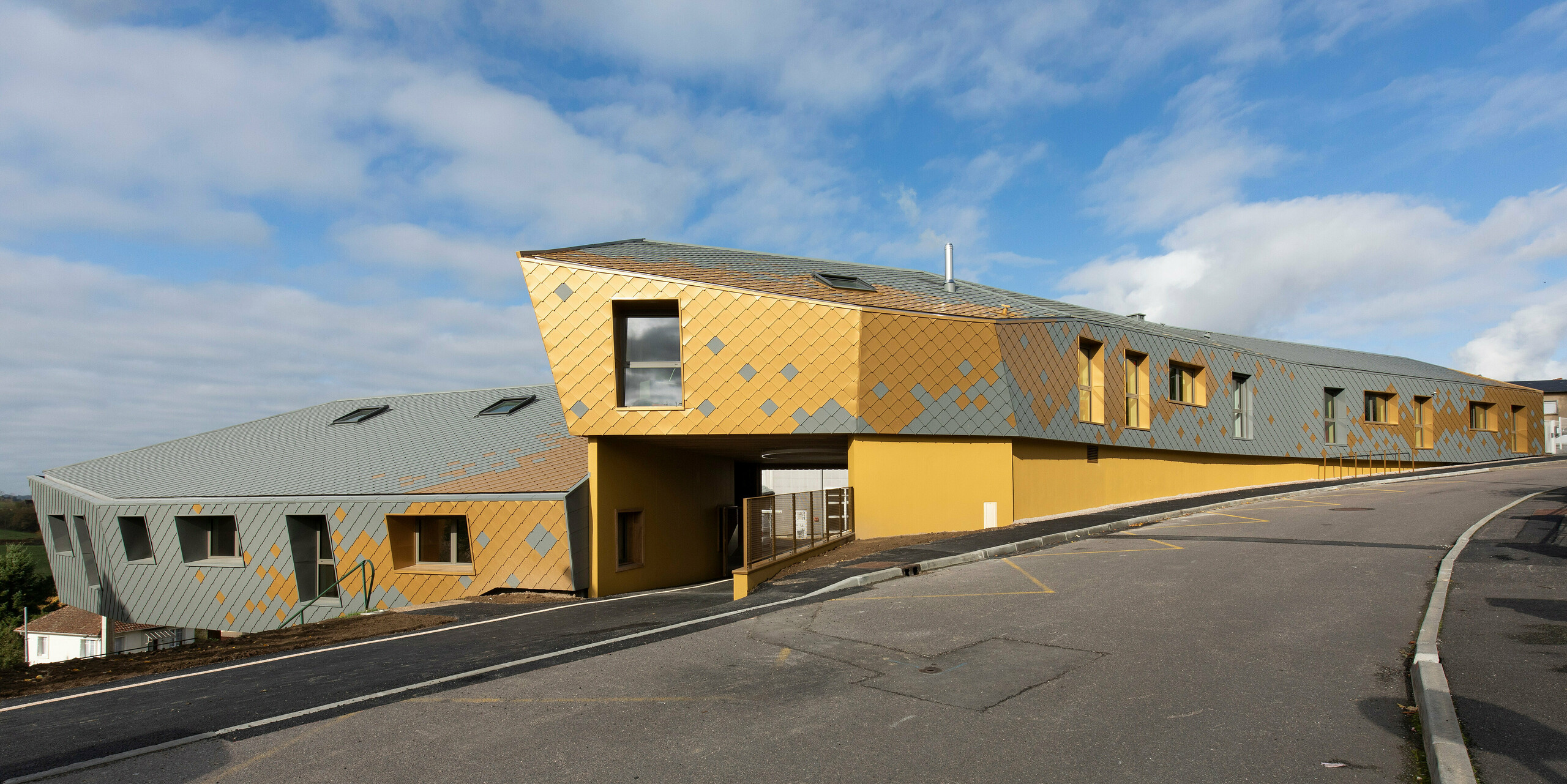 Photo de loin de l'école primaire de Pierre-Buffière avec de remarquables losanges de toiture et de façade PREFA 29 × 29 en gris souris P.10 et maya gold