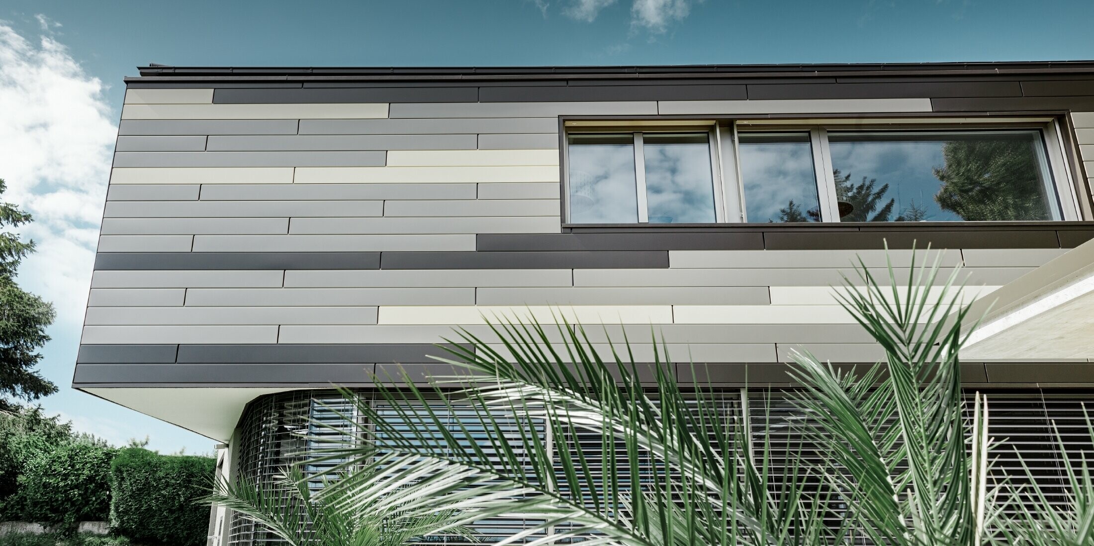 Modernes Einfamilienhaus mit Flachdach und überdachter Terrasse mit einer individuell gestalteten Aluminiumfassade aus Sidings in braun, bronze und elfenbein von PREFA