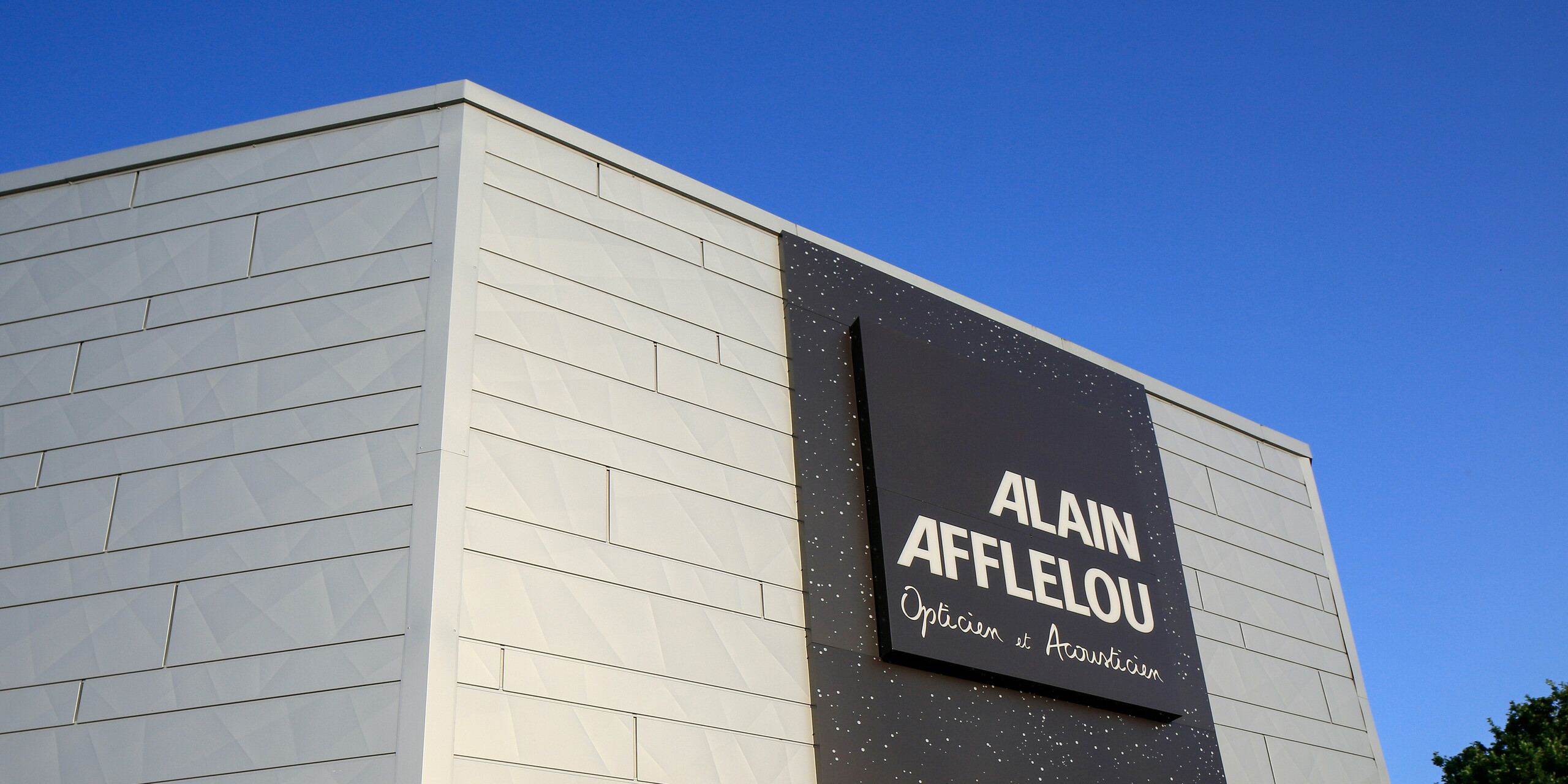 Zone d'entrée du magasin AFFLELOU à Auray avec une grande enseigne d'entreprise et une façade extravagante en PREFA Siding.X en argent métallisé