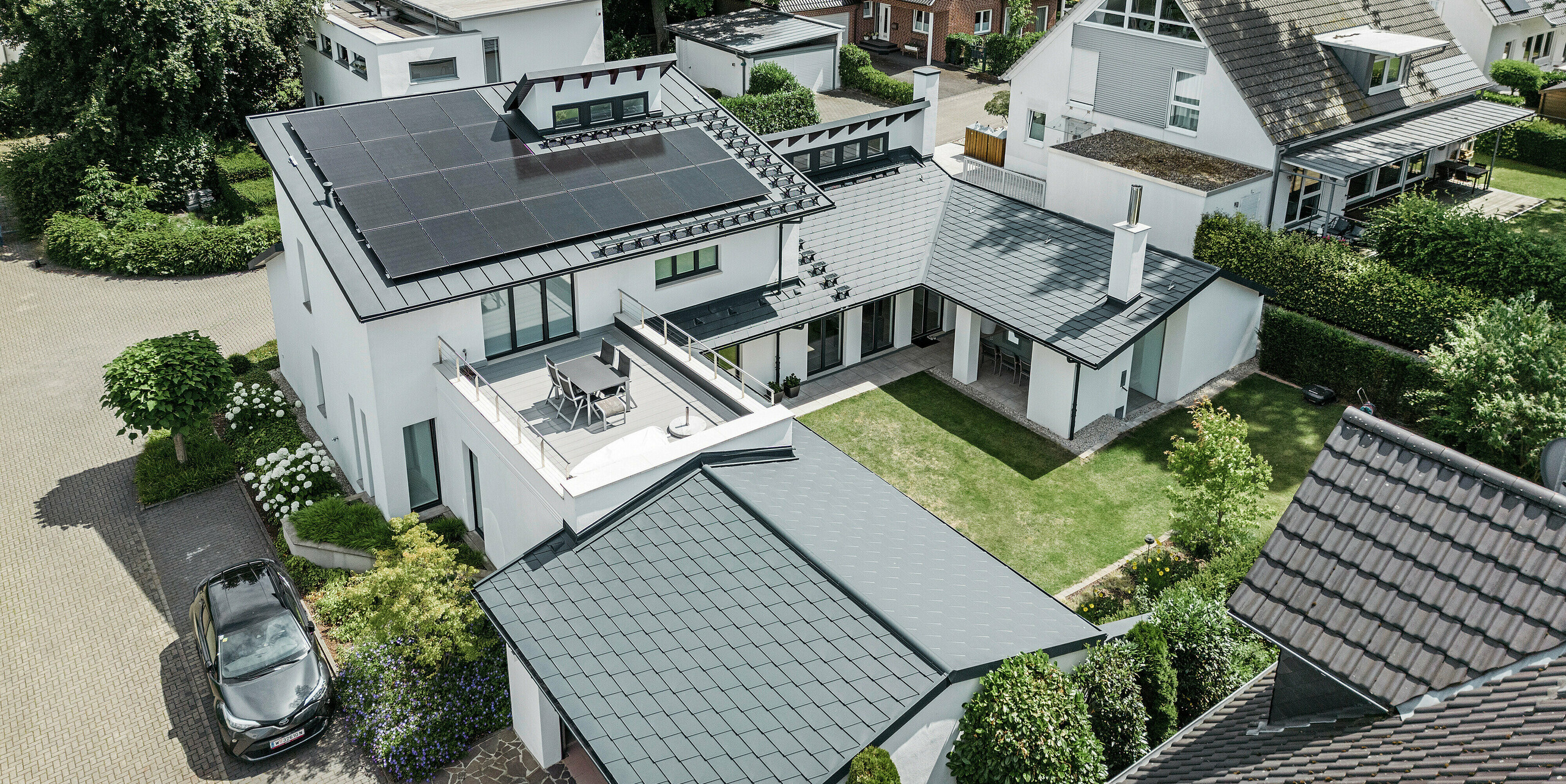 Vista a volo d'uccello dell'eccezionale paesaggio del tetto di una casa unifamiliare a Dortmund con scandola DS.19 PREFA e PREFALZ in P.10 antracite e un impianto fotovoltaico di grandi dimensioni.