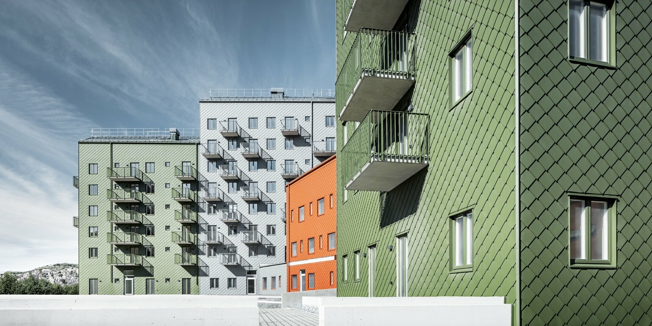 Mehrere Wohnhäuser nebeneinander, eingekleidet mit der PREFA Wandraute 29 × 29 in den Farben Ziegelrot, Olivgrün und Hellgrau.