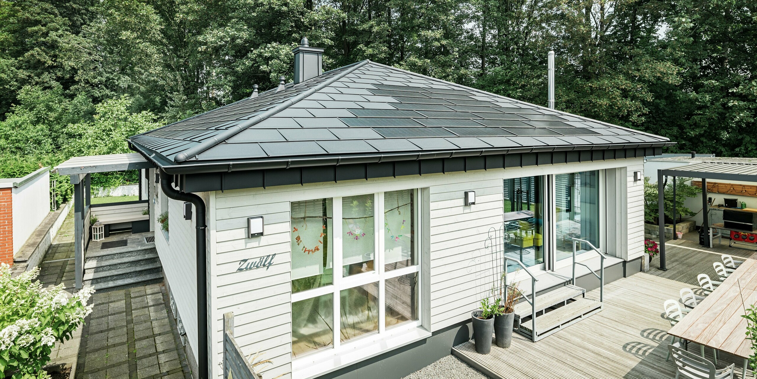 Moderner Bungalow in Rommerskirchen mit PREFA Aluminiumdach. Innovative PREFA Solardachplatten schützen das Haus und erzeugen gleichzeitig Strom aus nachhaltiger Sonnenenergie. Zusätzlichen Schutz bieten die robusten Dachplatten R.16. Die Dachentwässerung mit Saumrinne und Ablaufrohr sorgt für die nötige Funktionalität. Alle PREFA Aluminiumprodukte sind in der hochwertigen Farbbeschichtung P.10 Schwarz ausgeführt und sorgen so für ein elegantes Gesamtbild.